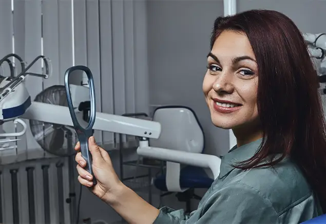 mujer en clínica dental sonriendo frente a un espejo